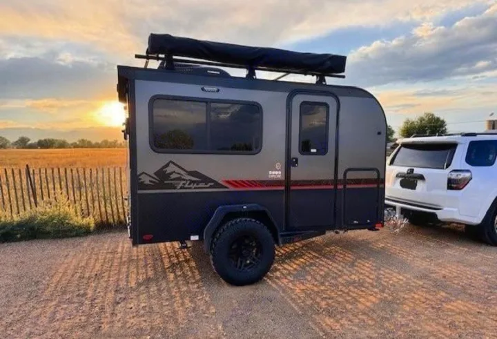 A dark gray rugged camping trailer, ideal for an RV rental, is hitched to a white SUV at sunset.. InTech RV Flyer 2023