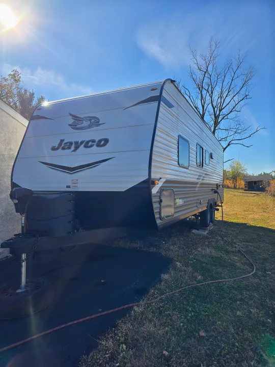A white and gray Jayco travel trailer is parked outside on a sunny day, hinting at your next rv rental adventure.. Jayco Jay Flight SLX 2022