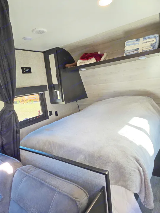Cozy RV rental bedroom with soft grey blankets, overhead shelves, and a large window.. Jayco Jay Flight SLX 2022