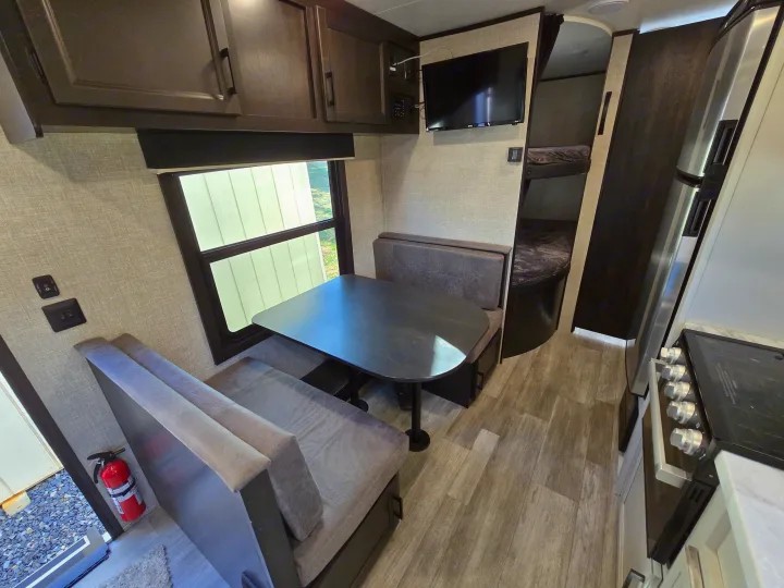 RV rental interior: dinette with window, overhead cabinets, adjacent kitchen area, and bunk beds.. Jayco Jay Flight SLX 2022