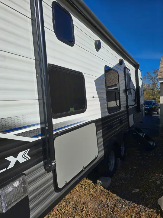 Side view of a modern RV rental parked outdoors, featuring white and black exterior, windows, awning, and storage.. Jayco Jay Flight SLX 2022