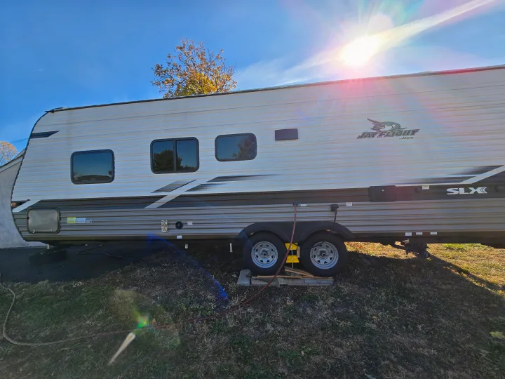 Side view of a Jayco travel trailer RV rental, parked outdoors on grass under a bright, sunny blue sky.. Jayco Jay Flight SLX 2022