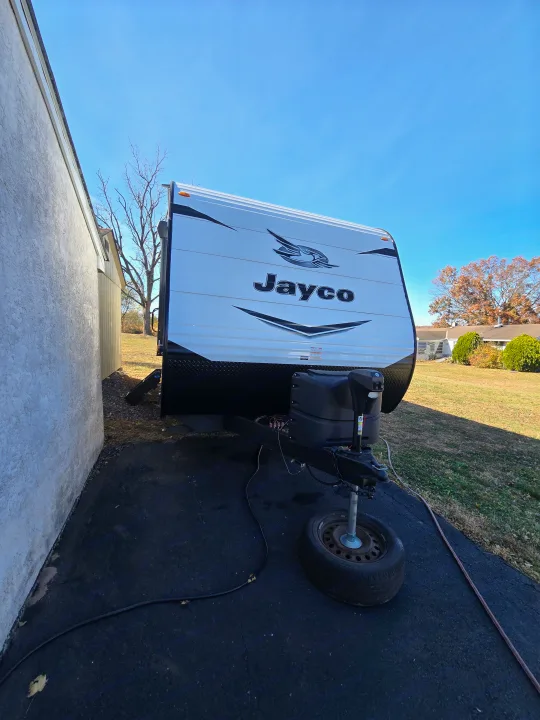 A white Jayco travel trailer, perfect for an rv rental, sits parked on asphalt next to a building under a blue sky.. Jayco Jay Flight SLX 2022