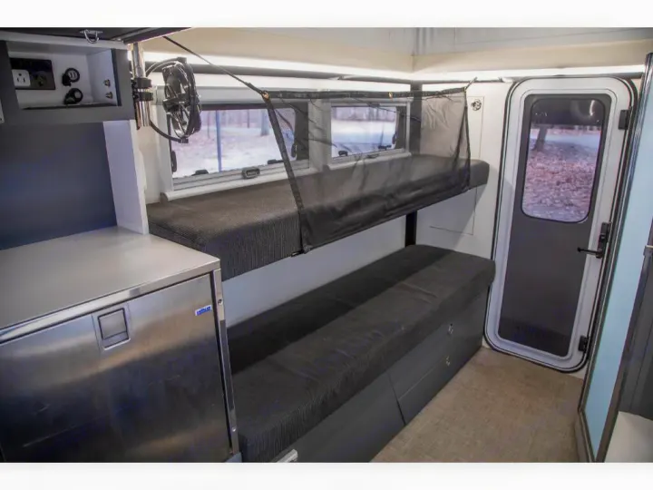 RV rental interior features sturdy bunk beds, safety net, a compact fridge, power outlets, and a door showing trees.. Bruder EXP-6 2018