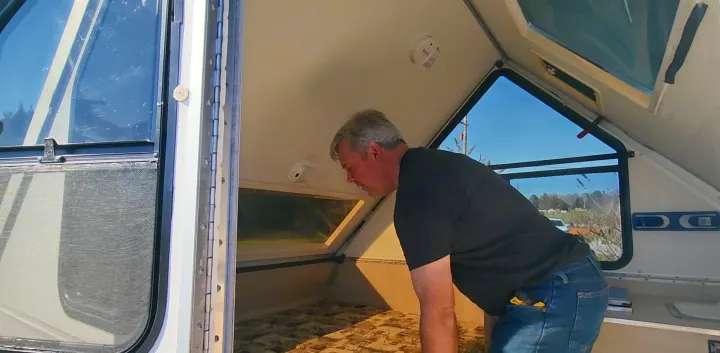 Man leans into an A-frame RV rental, inspecting its light interior. The compact camper features a bed area and numerous windows.. A Liner A Liner Popup Trailer 2006