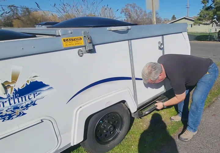 A man adjusts the side step on a white Sportliner pop-up RV rental, demonstrating pre-trip setup.. A Liner A Liner Popup Trailer 2006