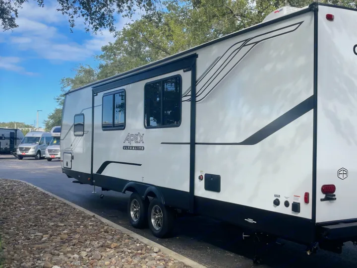 This large white Apex Ultralite travel trailer makes an excellent RV rental. Side view shows its awning, windows, and dual axles.. Coachmen APEX 284BHSS 2025