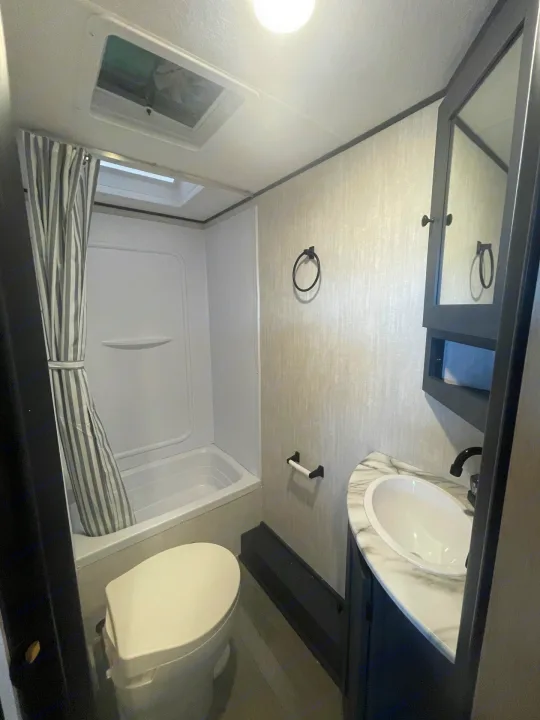 An RV rental's modern bathroom, featuring a white tub/shower, toilet, and sink vanity with a mirror.. Coachmen APEX 284BHSS 2025