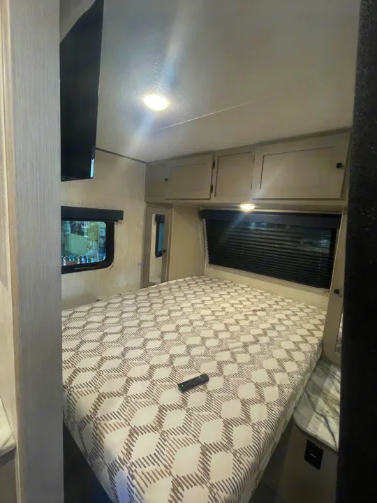 Cozy RV rental bedroom featuring a patterned bed, wall-mounted TV, and practical storage. Perfect for a comfortable journey.. Coachmen Apex 245 BHS 2025