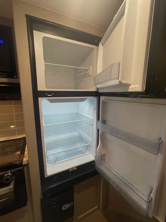 This empty, clean RV rental refrigerator, featuring top freezer and lower fridge with shelves and door storage.. Coachmen Apex 245 BHS 2025