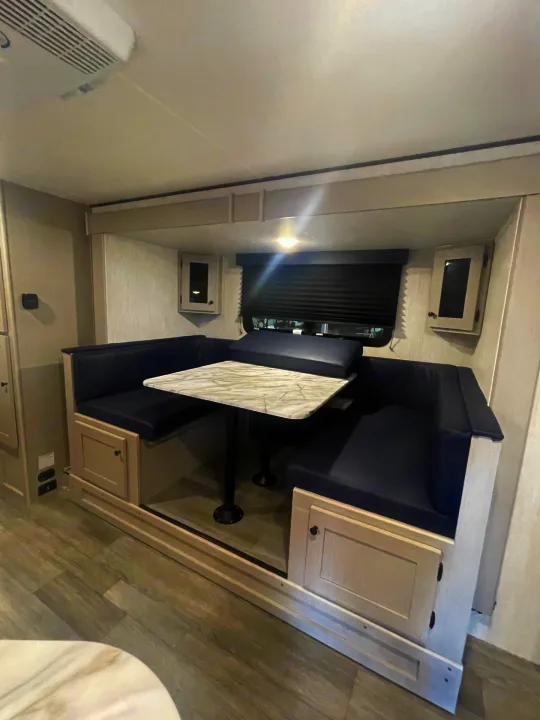 This cozy RV rental features a modern dinette with comfy blue benches, a table, and overhead cabinets, perfect for meals and relaxation.. Coachmen Apex 245 BHS 2025