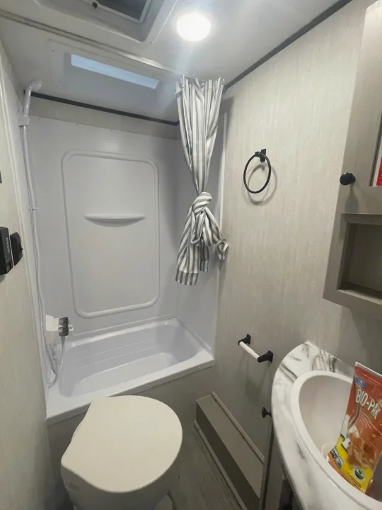 This RV rental features a functional bathroom with a compact tub/shower, toilet, and sink. Includes a skylight and striped curtain.. Coachmen Apex 245 BHS 2025