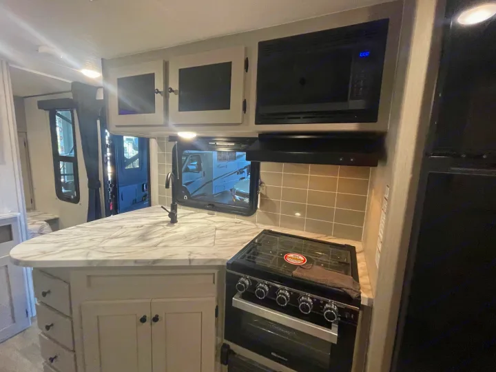 RV rental kitchen: modern light interior with a white-marbled counter, sink, stove, and microwave.. Coachmen Apex 245 BHS 2025