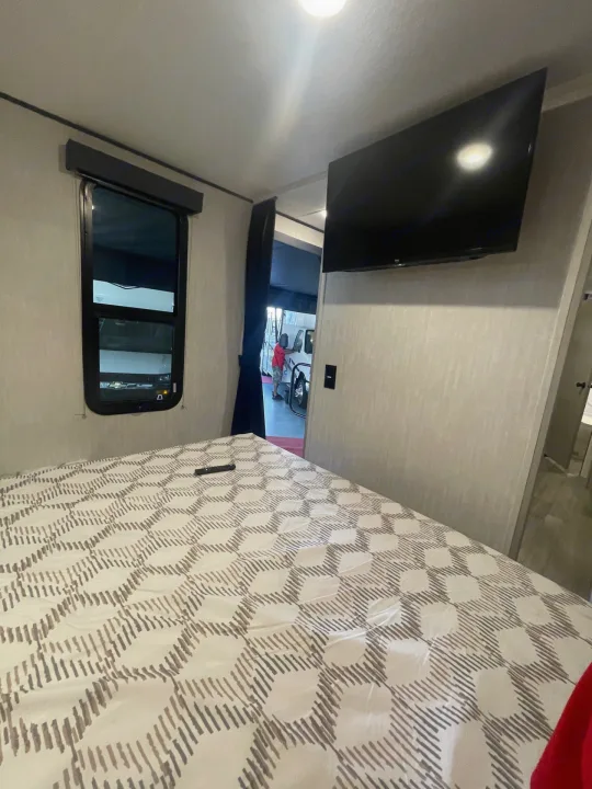 Modern RV rental bedroom interior: large bed, wall-mounted TV, and window with a view of another vehicle.. Coachmen Apex 245 BHS 2025