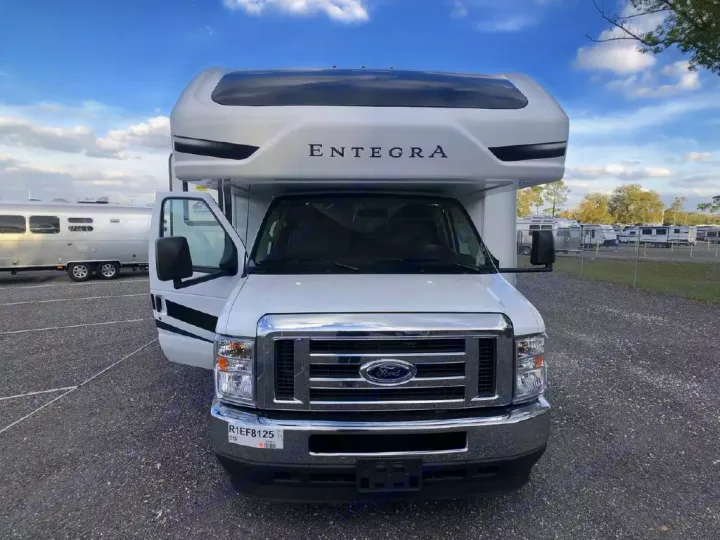 White Entegra rv rental, a Ford motorhome, parked on a gravel lot with its door open. Other RVs are in the background.. Entegra Coach Odyssey 2024