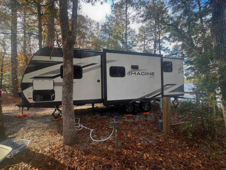 An Imagine XLS rv rental is parked at a beautiful wooded campsite beside a lake, ideal for your next outdoor adventure.. Grand Design Imagine XLS 2023