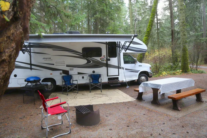 An RV rental provides a cozy campsite in a tranquil forest, complete with a picnic table, grill, fire pit, and chairs.. Jayco Greyhawk 2019