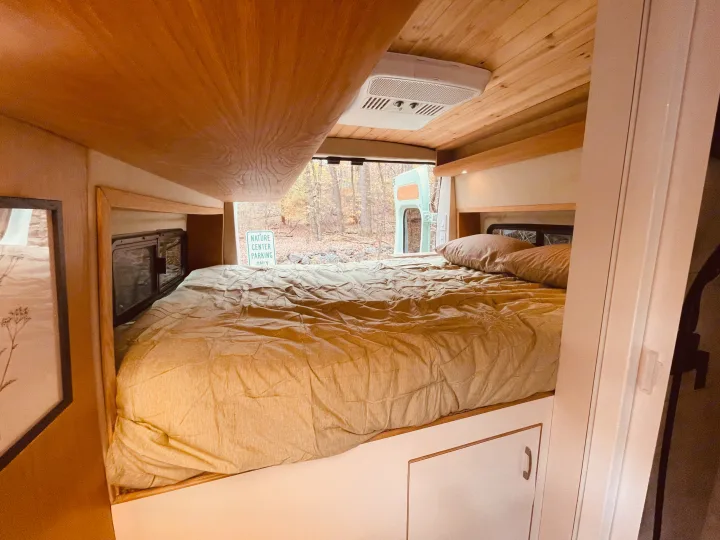 Cozy RV rental sleeping area with a comfortable bed, wood interior, and nature views from the back.. Dodge Pro Master High Roof 3500 Extended 2021