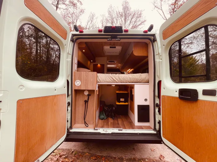 Step inside this rv rental camper van! Rear view showcasing its custom wood interior, raised bed, and accessible storage.. Dodge Pro Master High Roof 3500 Extended 2021