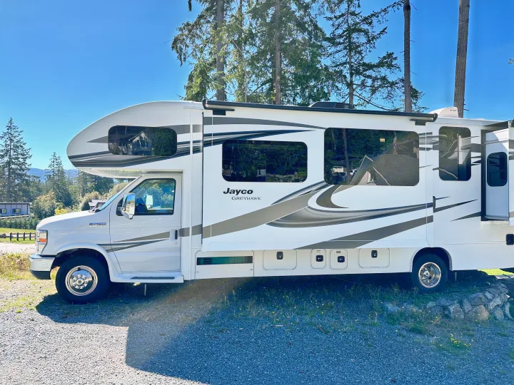 White Jayco Greyhawk RV rental parked amidst tall trees, ready for your next outdoor travel adventure.. Jayco Greyhawk 2019