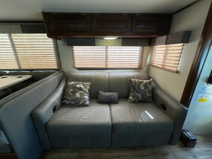This RV rental interior features a gray sofa, dinette booth, overhead cabinets, and pleated window blinds.. Forest River Fr3 2019