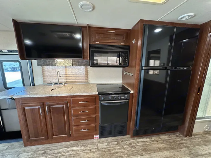 Explore this RV rental's modern kitchen: dark wood cabinets, black fridge, microwave, stove/oven, sink, and mounted TV.. Forest River Fr3 2019