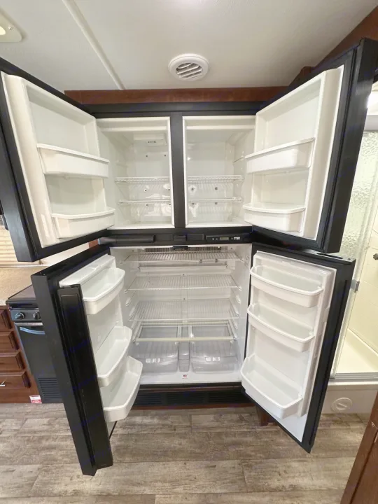 Clean & spacious rv rental refrigerator/freezer with all doors open, revealing shelves, clear bins, and door storage.. Forest River Fr3 2019