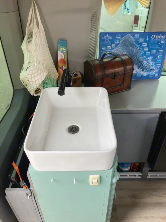 This RV rental's interior features a white sink, O'ahu map, and antique-style chest, ideal for travel.. Ford Transit 2018
