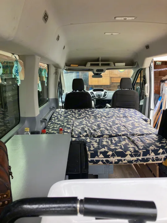 Cozy camper van interior with a patterned bed, ideal for an rv rental adventure. View from rear to front seats.. Ford Transit 2018