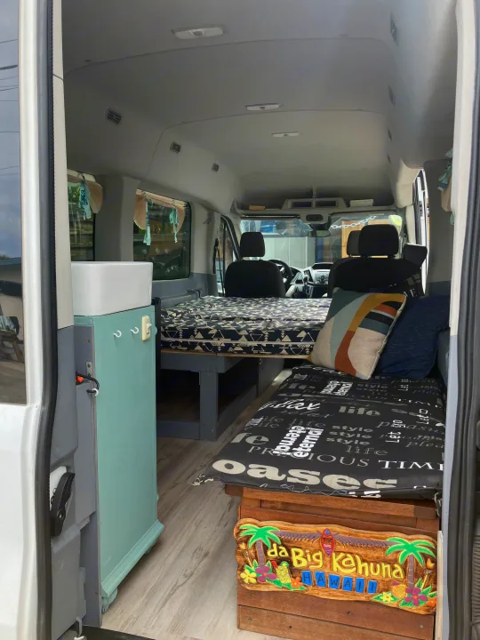 RV rental van conversion interior: a cozy space with a bed, sink, and seating area featuring a Hawaiian theme.. Ford Transit 2018
