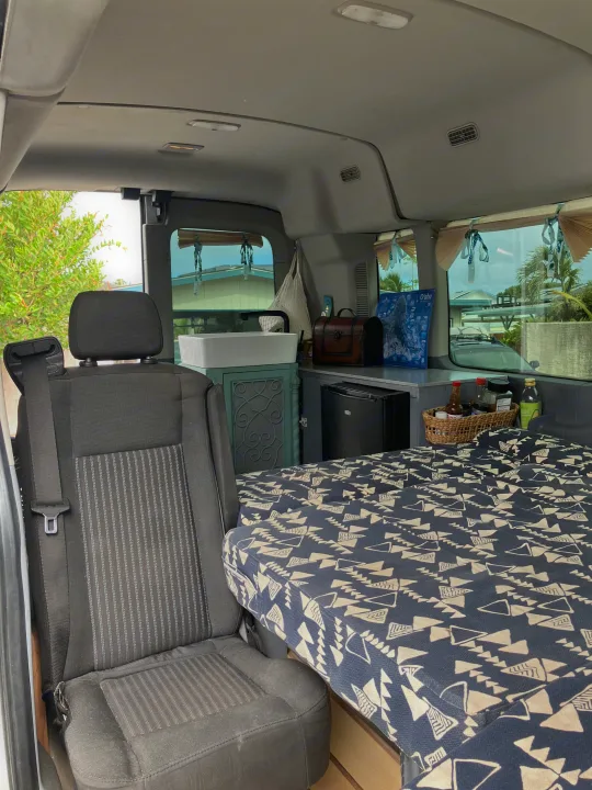 Inside this RV rental: a compact camper van interior with patterned bed, sink, fridge, and seating for your next adventure.. Ford Transit 2018