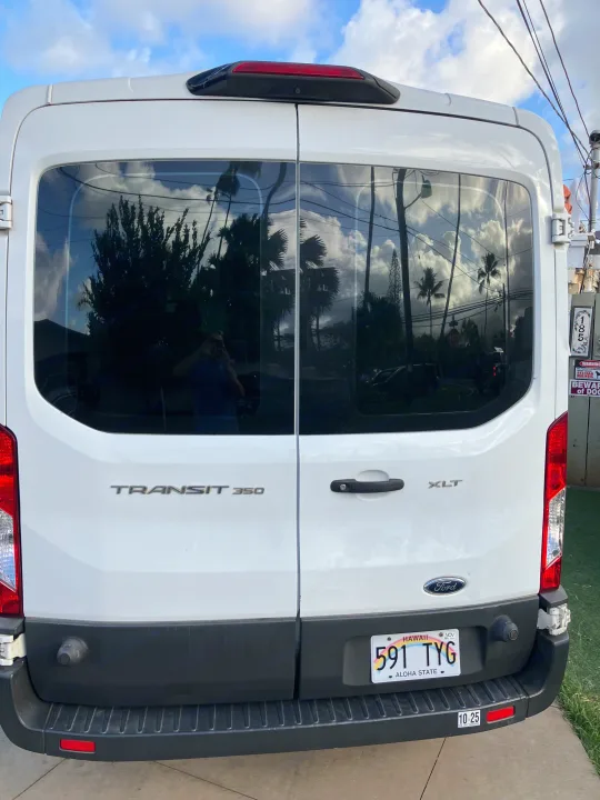 Rear view of a white Ford Transit 350 rv rental van, parked, with a Hawaii license plate and reflections in windows.. Ford Transit 2018