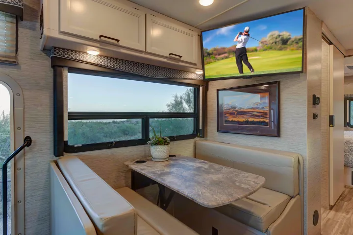Experience comfort in this RV rental's dinette, featuring plush seating, a TV, and a scenic window with desert views.. Thor A.C.E. 2022