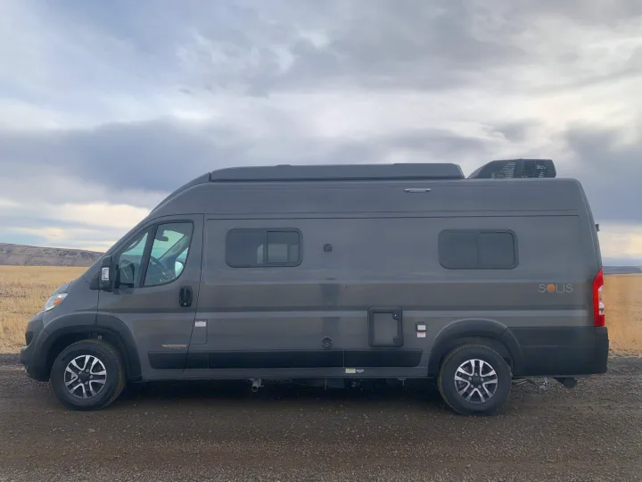 Grey Winnebago Solis camper van, ideal for RV rental adventures. Parked in a scenic field under cloudy skies.. Winnebago Solis 59PX 2025