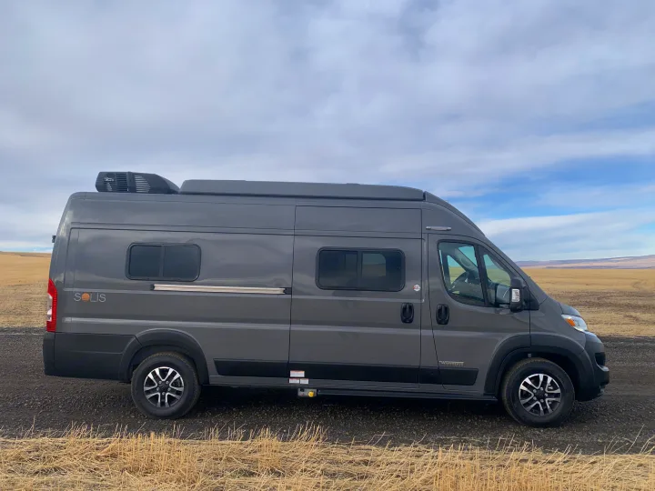 A sleek gray Winnebago Solis camper van, perfect for RV rental adventures, parked in a vast dry field under a cloudy sky.. Winnebago Solis 59PX 2025