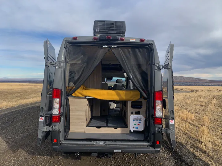 Open rear doors of a grey camper van RV, revealing a cozy interior with bed & utility panel. Ideal for an RV rental adventure.. Winnebago Solis 59PX 2025