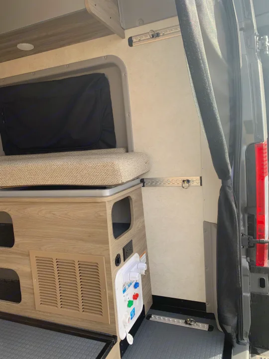 RV rental interior: A comfy camper van space featuring a bed, storage, power outlets, water hookups, and L-track for secure travel.. Winnebago Solis 59PX 2025