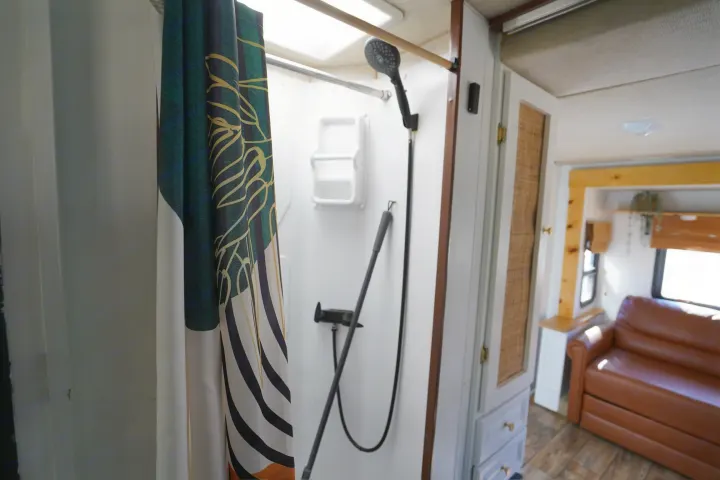 This RV rental features a compact shower with a dark green curtain, opening to a cozy living area with a leather sofa.. Jamboree Sport 2011