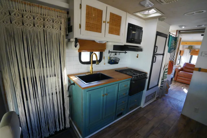Renovated rv rental kitchen showcasing teal cabinets, wood counters, and a unique macrame screen. Stylish and functional RV interior.. Jamboree Sport 2011