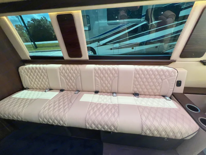 Inside a luxury RV rental: cream quilted leather bench seat with seatbelts, large windows reflecting another RV.. Midwest Automotive Designs Day Cruiser 2024