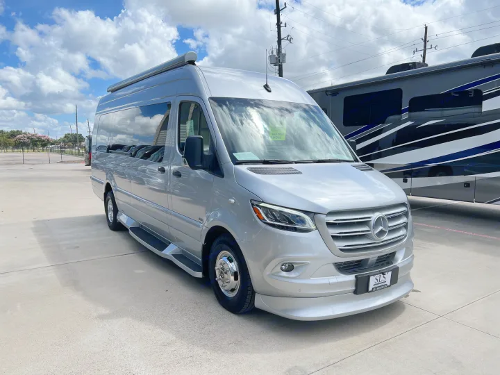 A silver Mercedes-Benz Sprinter van, suitable for RV rental, parked on a concrete lot under a blue, cloudy sky.. Midwest Automotive Designs Day Cruiser 2024