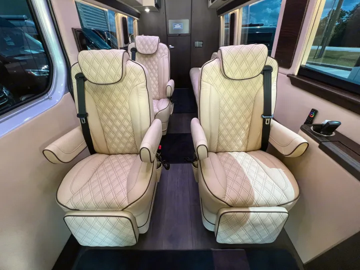 Luxury RV rental interior: Four cream-colored, diamond-quilted leather captain's chairs, wood floor, and modern controls.. Midwest Automotive Designs Day Cruiser 2024
