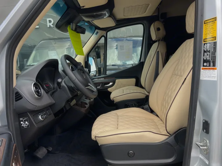 Modern RV rental interior: cream diamond-stitched seats, steering wheel, and dashboard details visible. Important wheel care warnings.. Midwest Automotive Designs Day Cruiser 2024