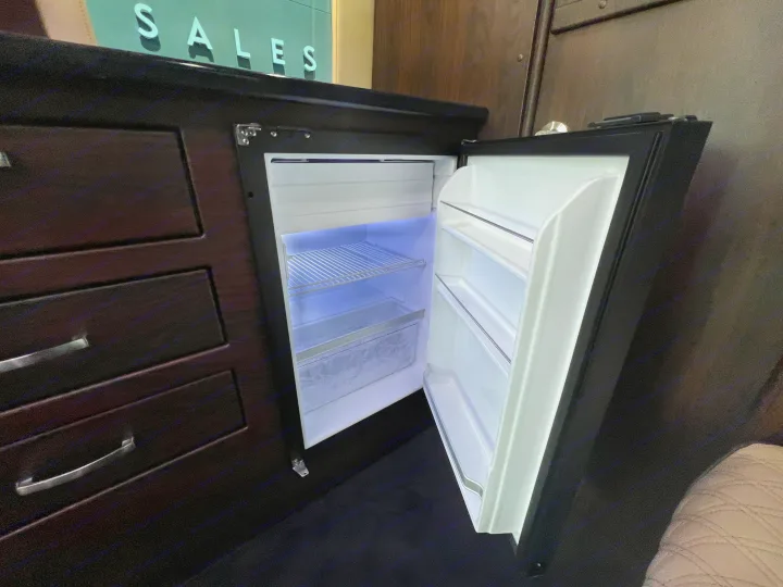 Inside an RV rental: a bright, open mini-fridge built into dark cabinetry alongside storage drawers.. Midwest Automotive Designs Day Cruiser 2024