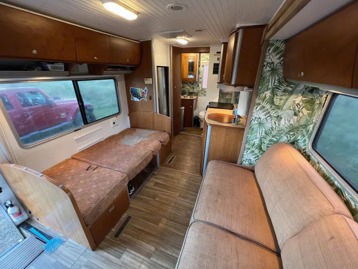 Bright rv rental interior featuring a versatile living/sleeping area, well-equipped kitchenette, and accessible bathroom. Palm print accents add flair.. Winnebago View 2005