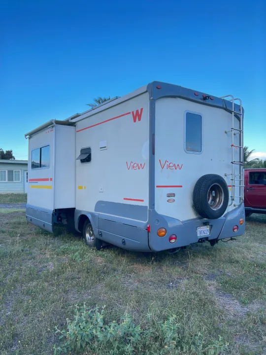 Rear 3/4 view of a white Winnebago View RV, slide-out extended, parked on grass. Perfect for an RV rental vacation!. Winnebago View 2005