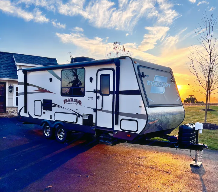 A white Starcraft Travel Star RV parked on a driveway with a vibrant sunset and tractor in the background, great for RV rental.. Starcraft Travel Star 2015