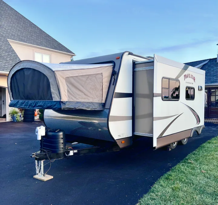 Modern white & gray hybrid RV rental with extended tent and slide-out sections, parked on an asphalt driveway near a house.. Starcraft Travel Star 2015