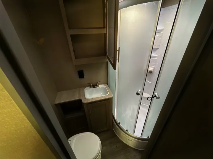 This RV rental's compact bathroom features a toilet, sink, vanity, and a corner shower with frosted doors.. Coachmen Catalina 2022