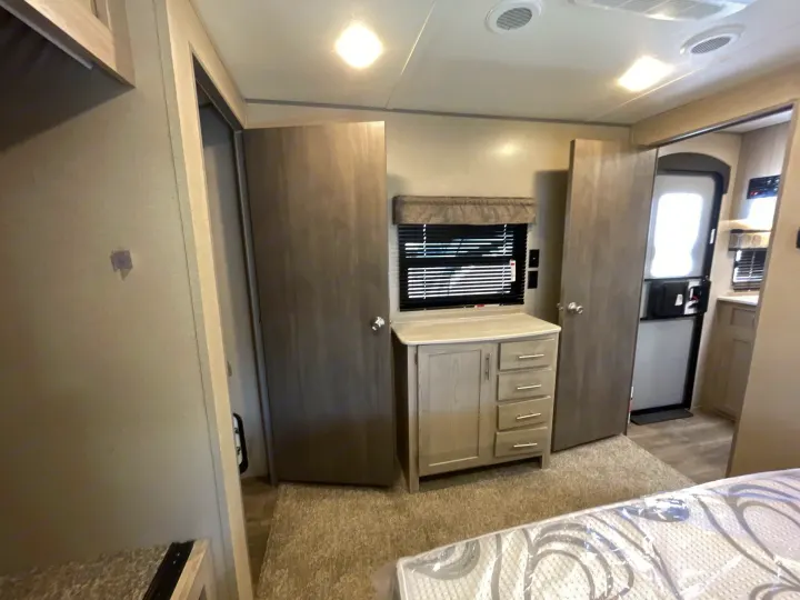 RV rental interior: a neatly arranged bedroom area featuring a new mattress, a dresser with a window, and open interior doors.. Coachmen Catalina 2022